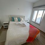 Cama de casal com coberta branca e almofadas.