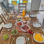 Sala de jantar da casa de praia em porto covo com close na mesa de madeira com sucos, pães e frutas.